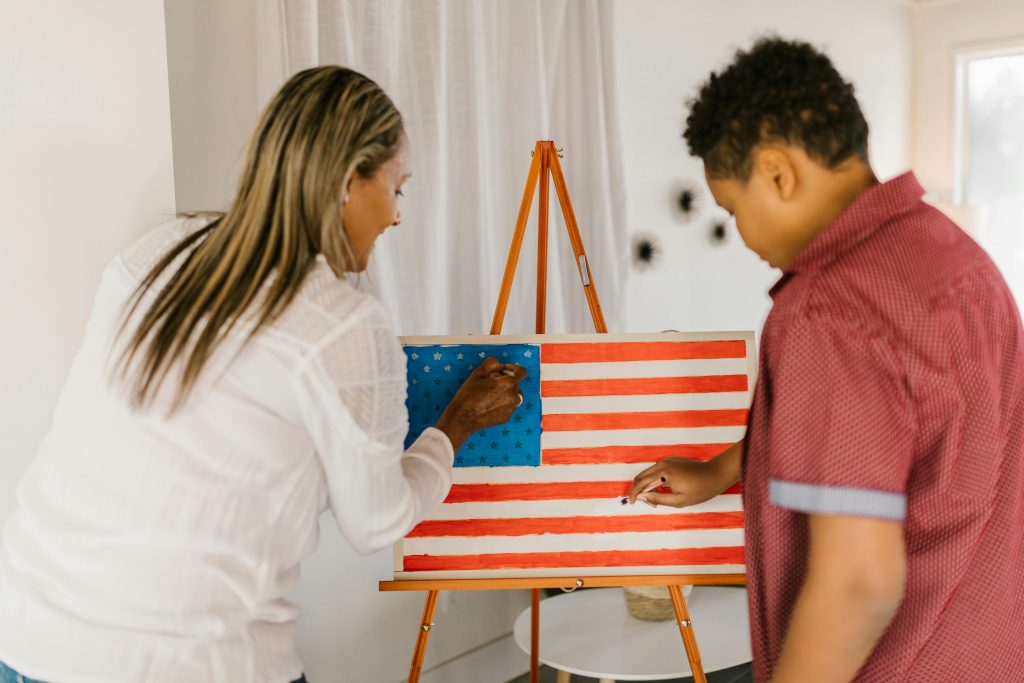 A mother and son engage in a painting activity at home, creating an American flag on canvas.